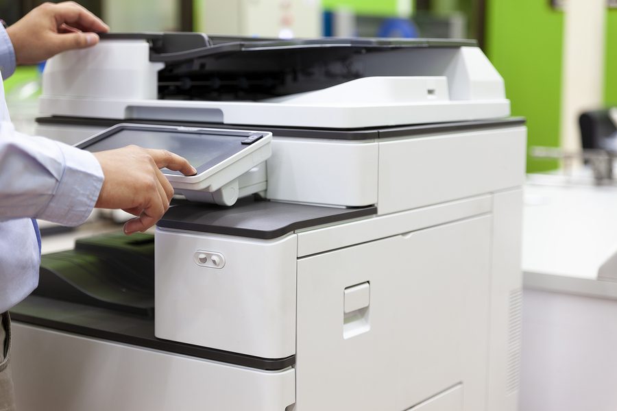 An all-in-one fax machine and printer being used by an employee in an office.