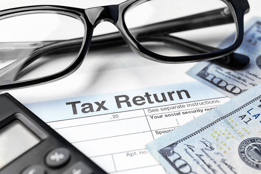 Tax return documents with a pair of glasses and some money.