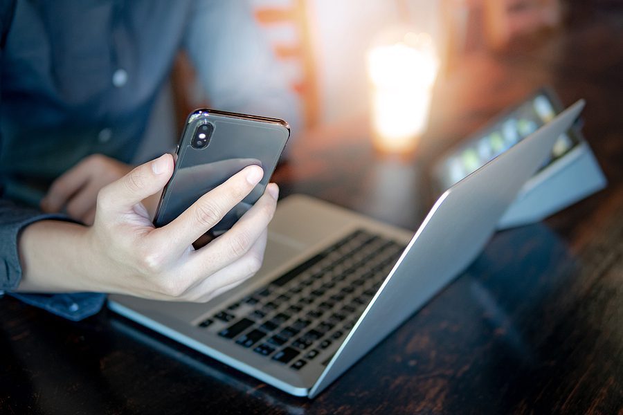 Man holding smartphone using a laptop.