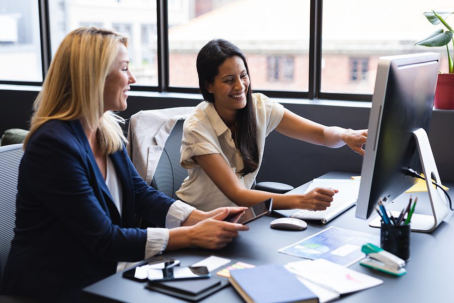 Two business women working in a modern business office near a large window.