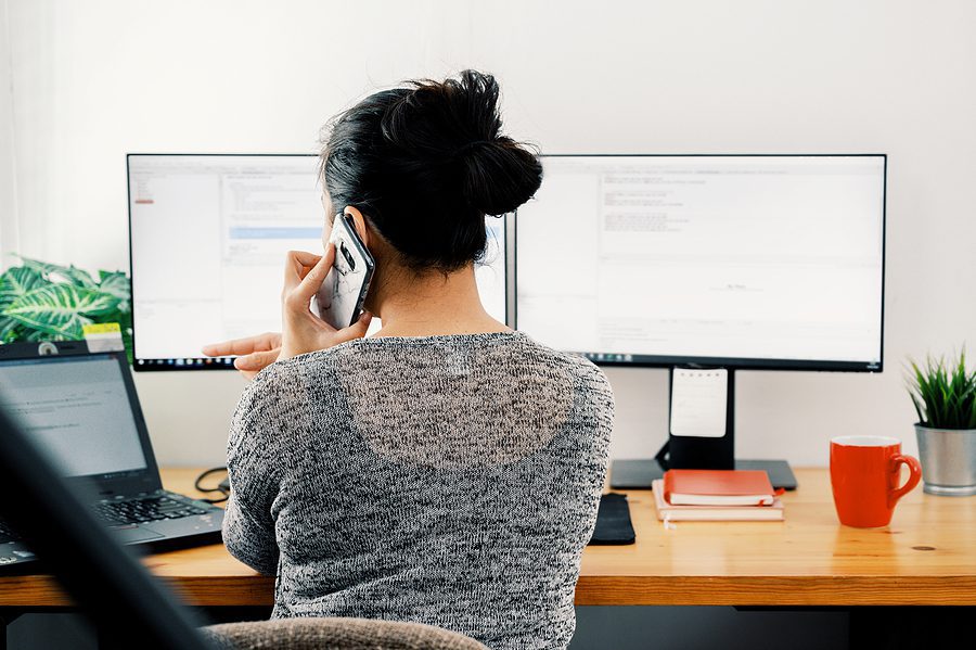 Woman working from home on a computer with two monitors. 