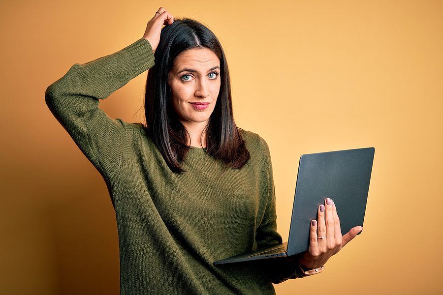 Woman scratching her head holding a laptop, confusion concept.