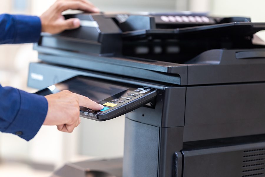 Business man's hands in blue suit pressing buttons on a printer, scanner, copy machine in an office