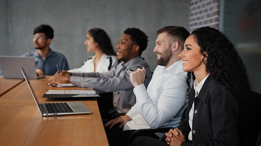 multiracial men and women employees sitting in conference room smiling with laptops in front of them