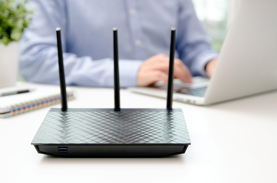 Close up of a wireless router with a man on a laptop behind it. 