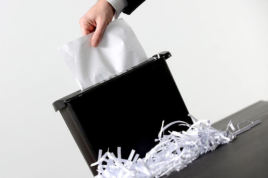 Hand of businessman putting a document in paper shredder with pile of previously shredded paper. 