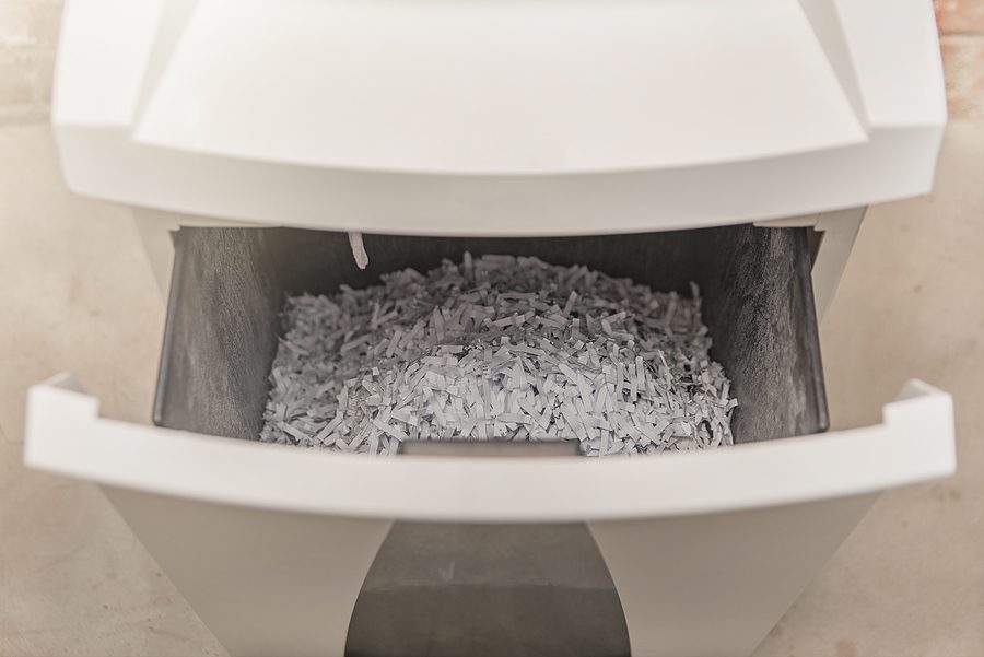 Close up of a white industrial paper shredder with shredded paper inside the basket. 