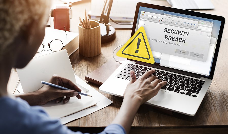 Woman using a laptop that has a "Security Breach" warning on the screen with a yellow triangle. 