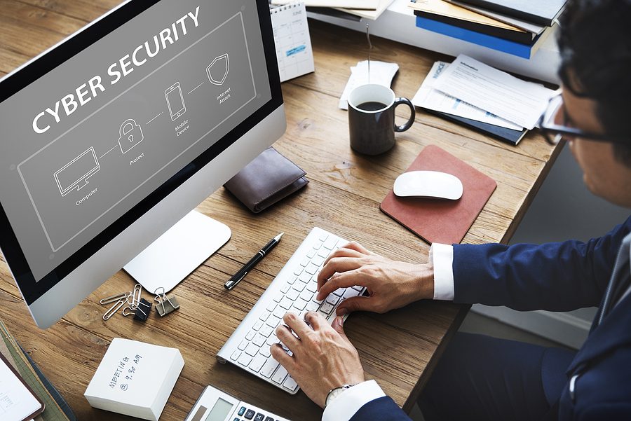 Man in suit typing on a computer in his office, with "Cyber Security" on the screen. 