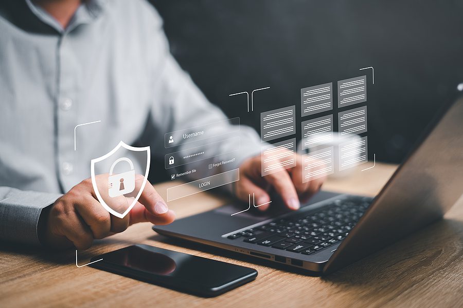 Closeup of a man at work, using his laptop and phone for extra security verification. 