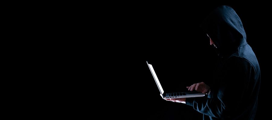 Cyber attack, dark web concept of a man in a hoodie holding a laptop against a black background. 