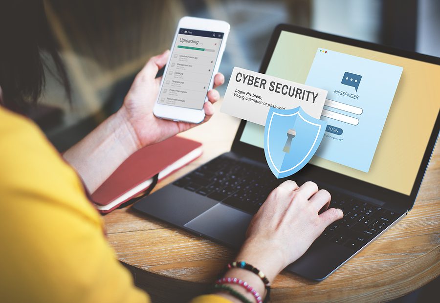 Female office worker holding her phone while trying to login to her computer that says "Cyber Security" on the screen. 