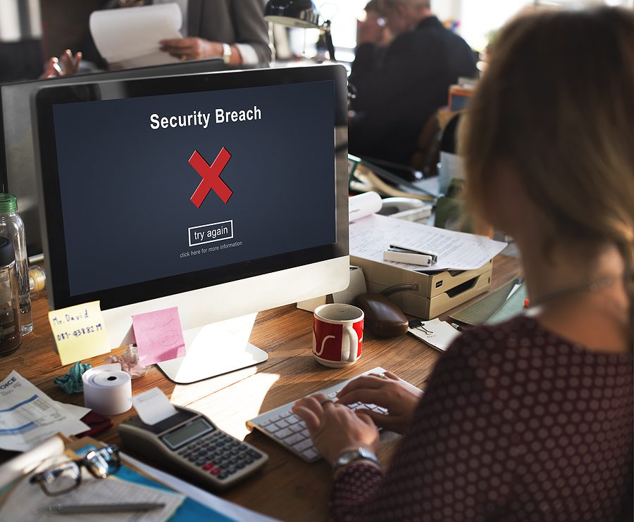 Female worker sitting at desk and staring at computer with "Security Breach" on the screen. 