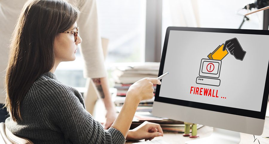 Woman pointing at her computer screen at work that says "Firewall" on it.