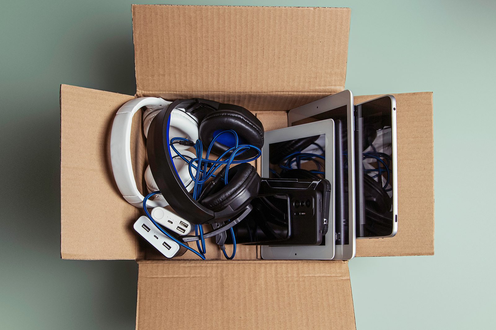 Cardboard box full of old used laptop computers, digital tablets, smartphones, power bank for recycling on gray background. Donation, e-waste, electronic waste for reuse, refurbish and recycle concept