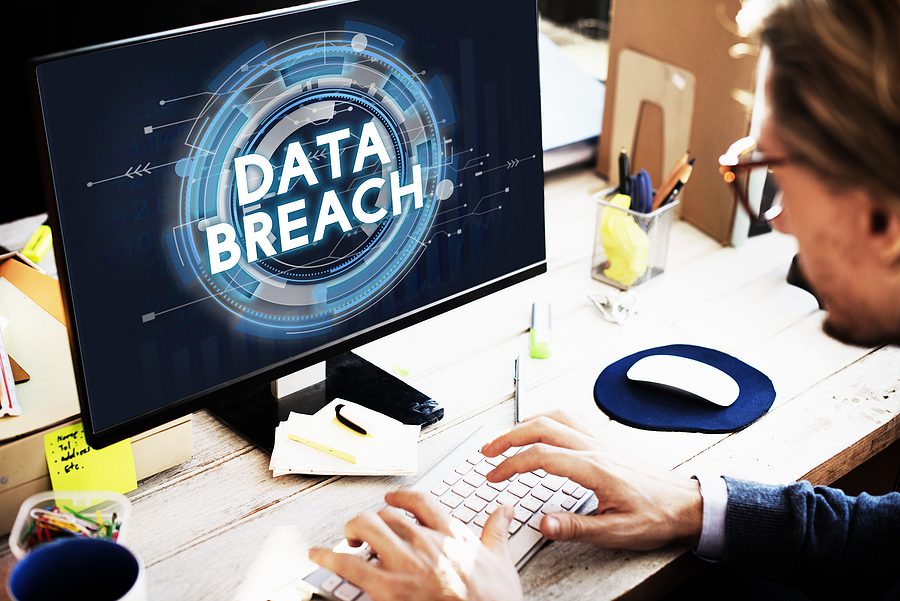 Man sitting at desk in his office with "Data Breach" on his computer screen 