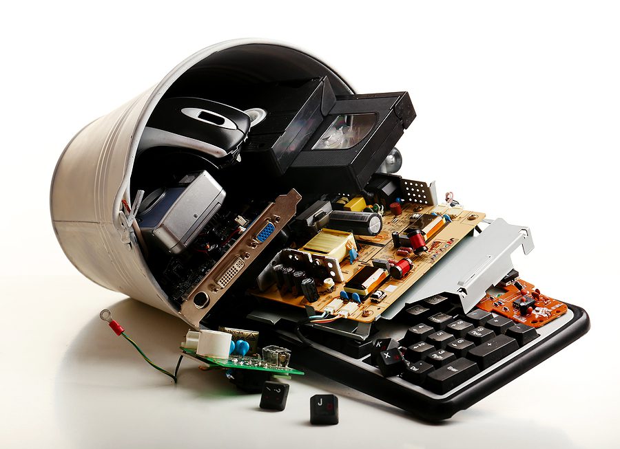 Old electronics in a trash can tipped over on a white background. 